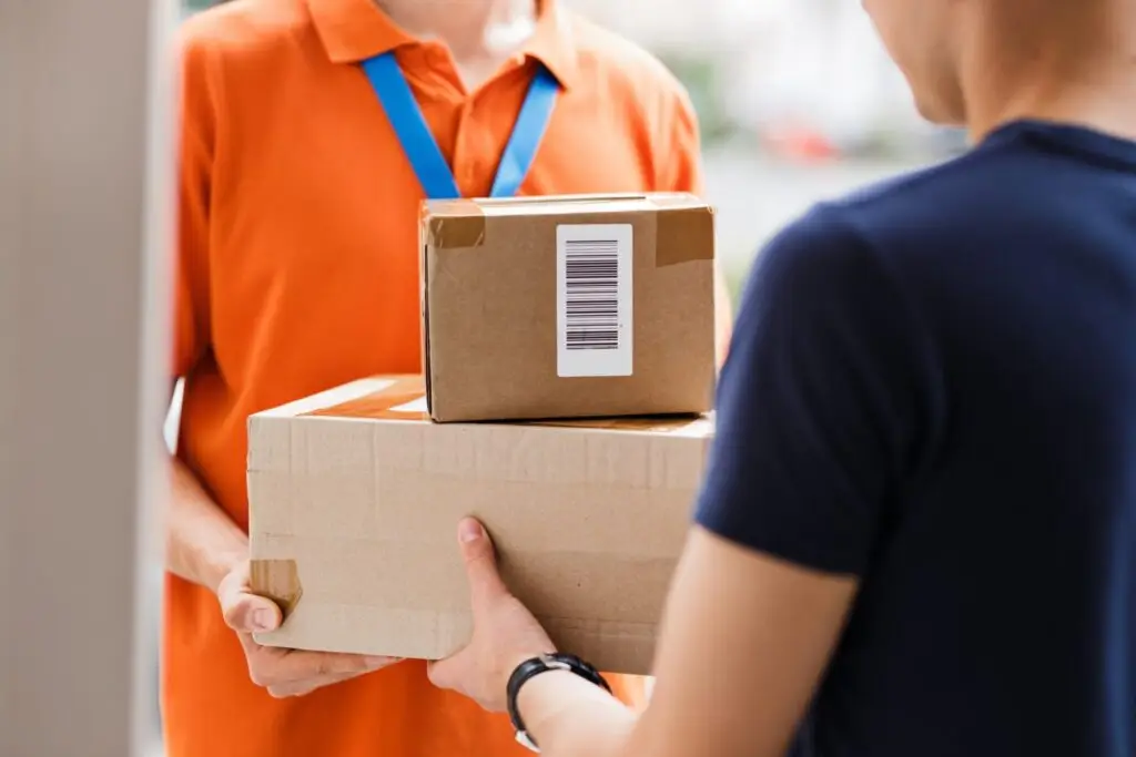 A person wearing an orange T-shirt and a name tag is delivering parcels to a client. Friendly worker