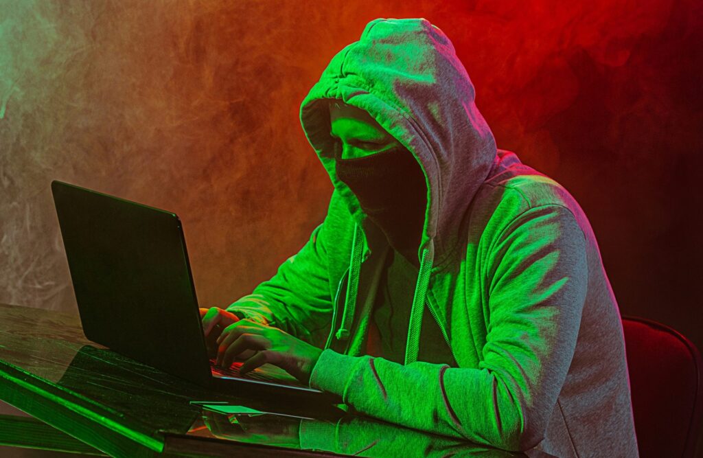 Hooded computer hacker stealing information with laptop